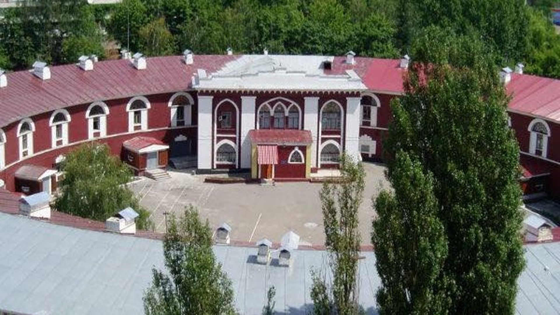 Червона будівля з білим фасадом, арочними вікнами та внутрішнім подвір'ям