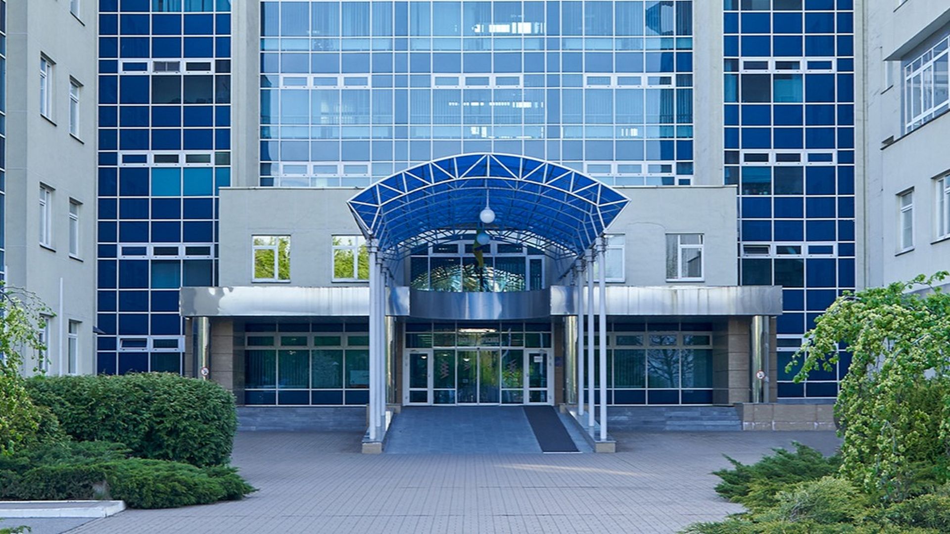 Сучасна будівля з великими скляними вікнами та синім навісом над входом