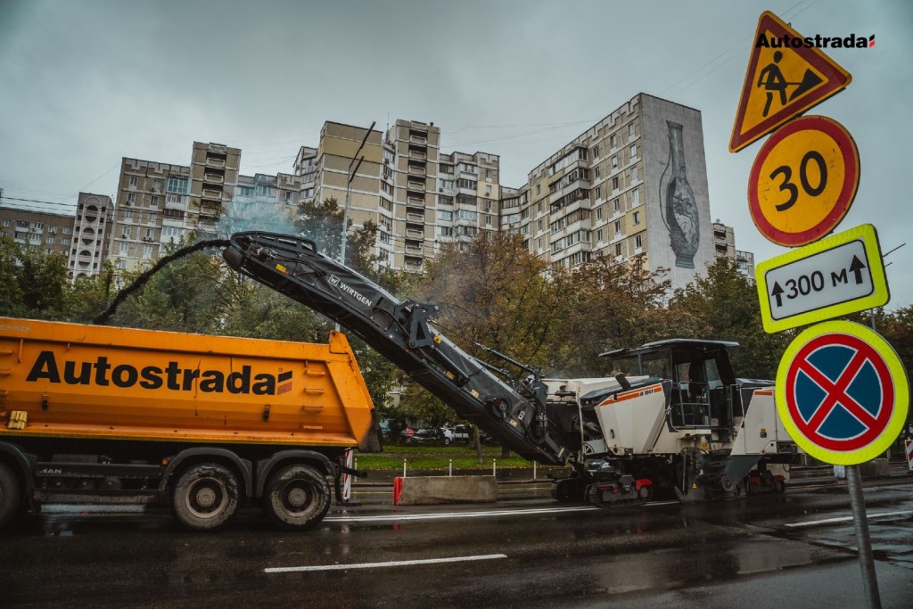 Дорожня фреза Wirtgen завантажує знятий асфальт у вантажівку Autostrada на фоні житлових будинків