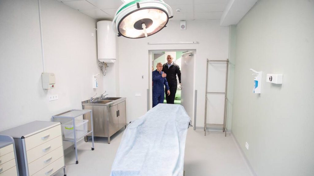 Операційна кімната, посередині операційний стіл, вхід у кімнату відкритий, у дверях стоїть мер Києва Кличко і ще один чоловік 