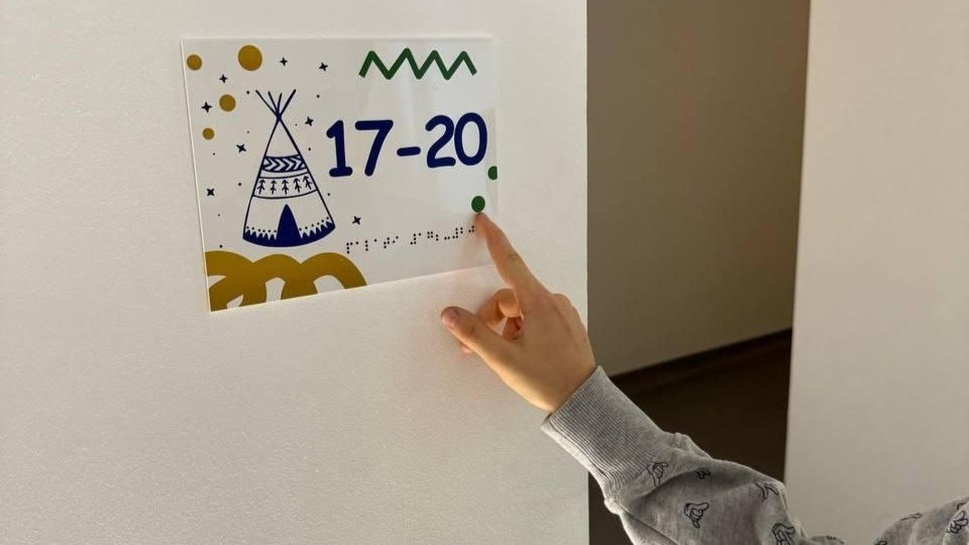 Дитяча рука, біля стіни з картинкою, на якій шрифтом брайля написаний зміст картинки