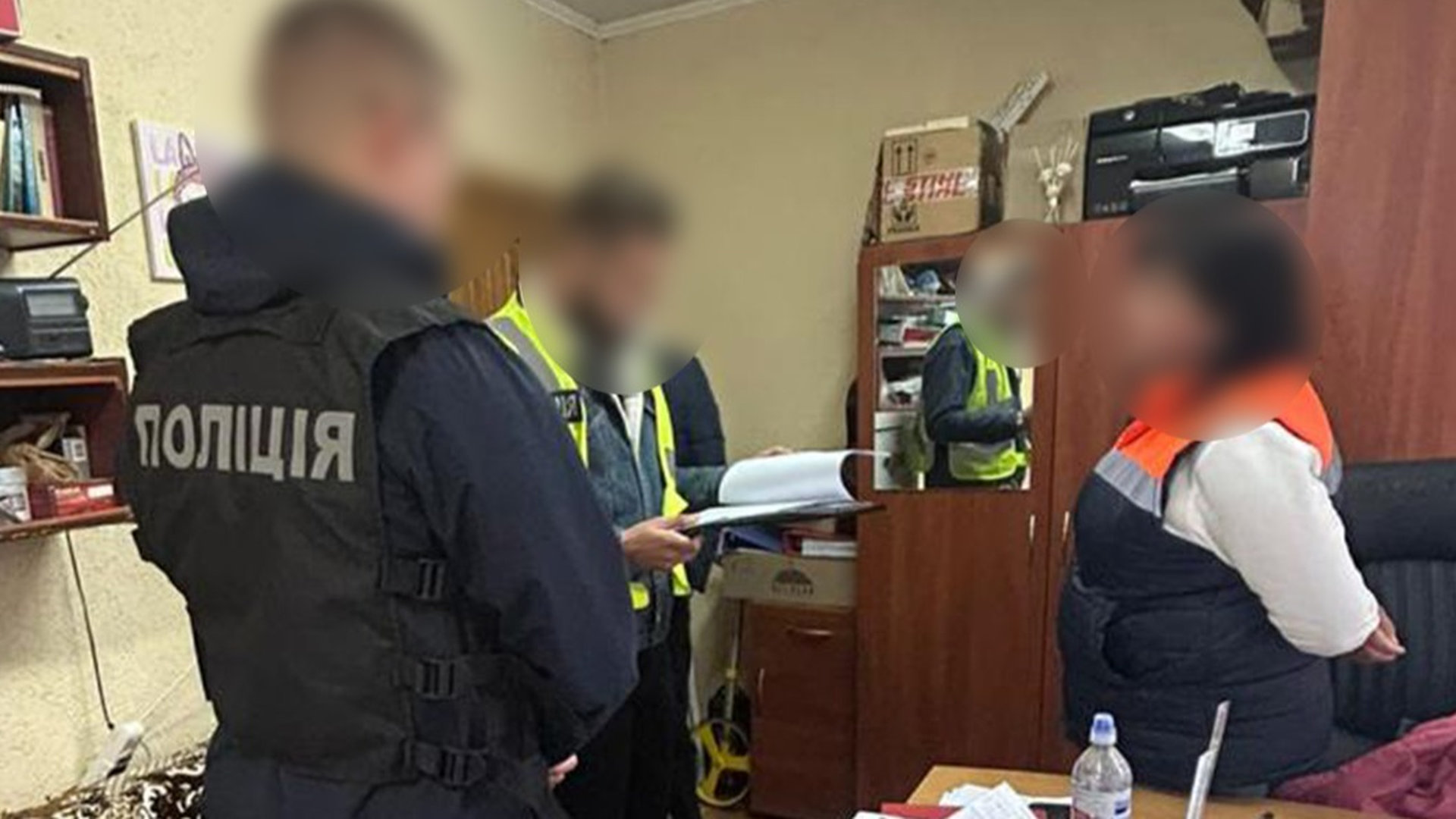 троє людей в кімнаті, двоє працівників поліції вручають підозру працівниці комунального підприємства