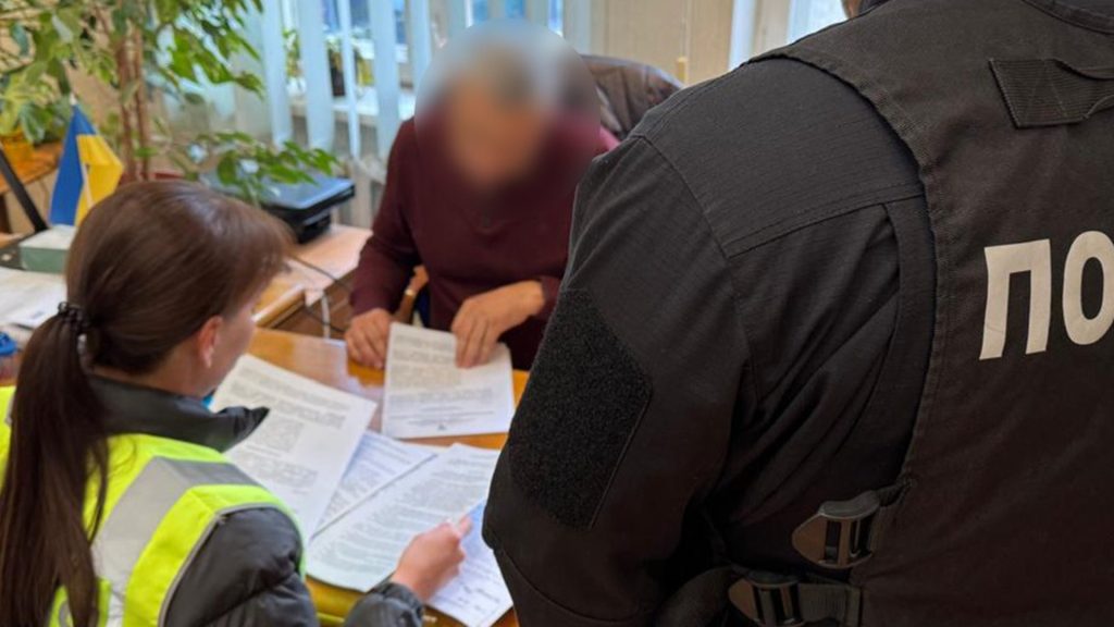 Двоє працівників полції спілкуються в кабінеті з чоловіком, який сидить за столом і щось підписує 