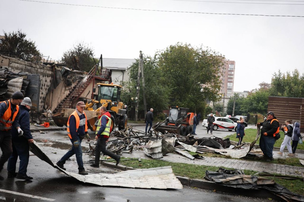 Комунальники в помаранчевих жилетах прибирають уламки та сміття після обстрілу, поряд працює спецтехніка