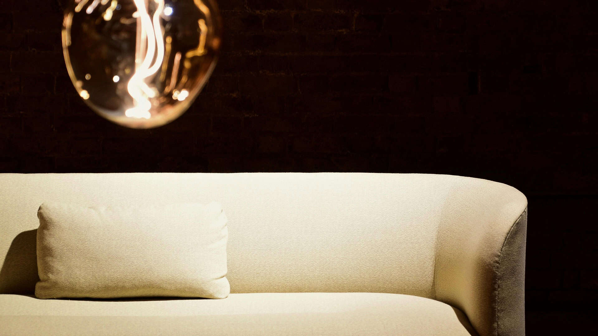 Білий диван на фоні темноти і над диваном горить одна лампа