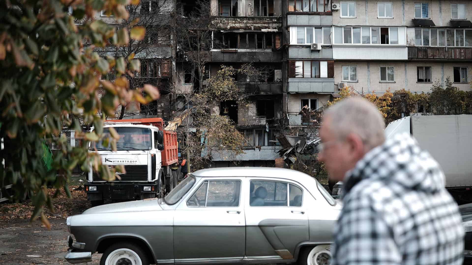 Чоловік проходить повз зруйнованої багатоповерхівки у Києві, біля будинку стоїть вантажівка, яка вивозить будівельні завали після прильоту