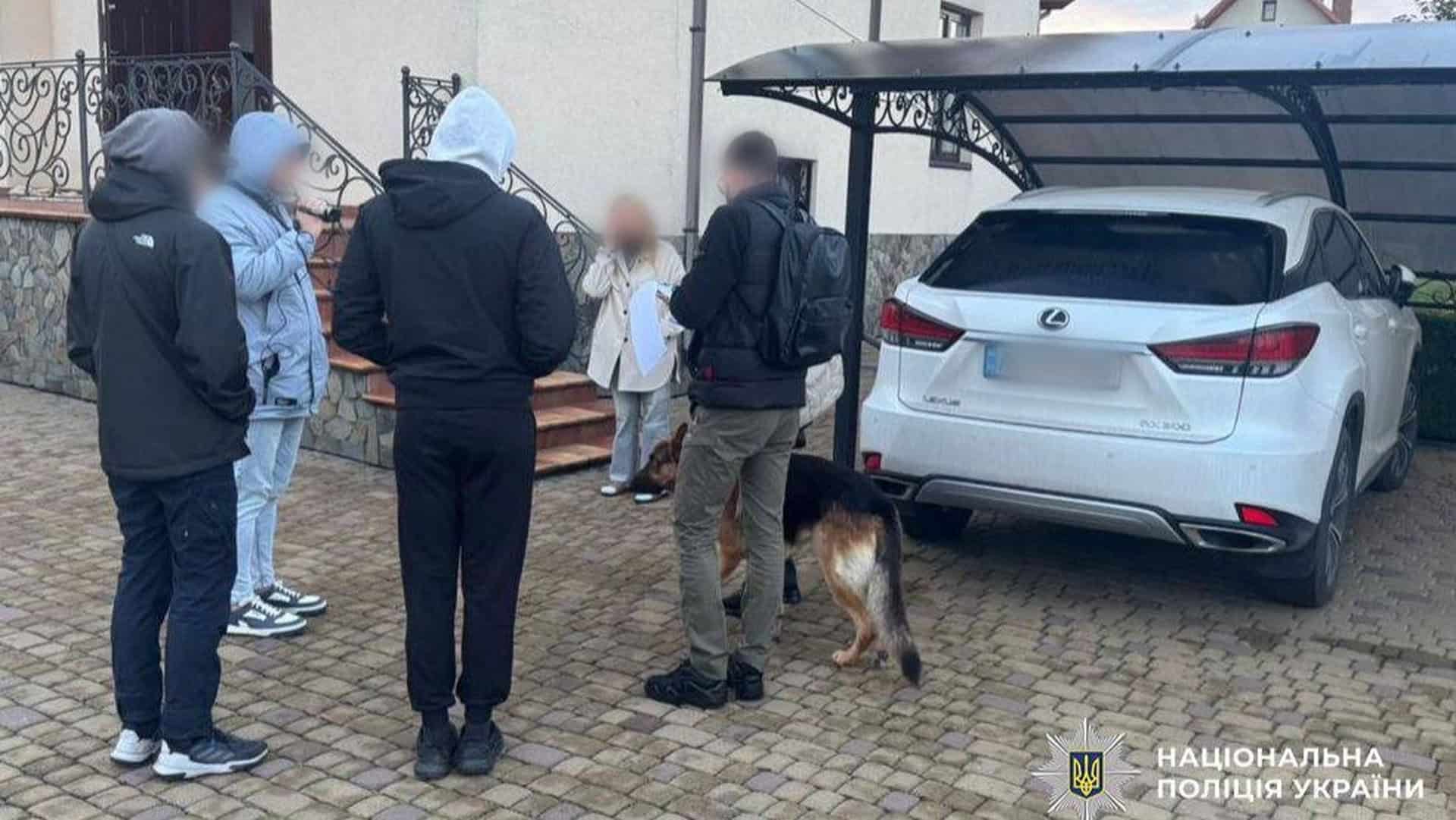 Слідчі дії біля приватного будинку: кілька осіб у верхньому одязі стоять поруч із білим автомобілем