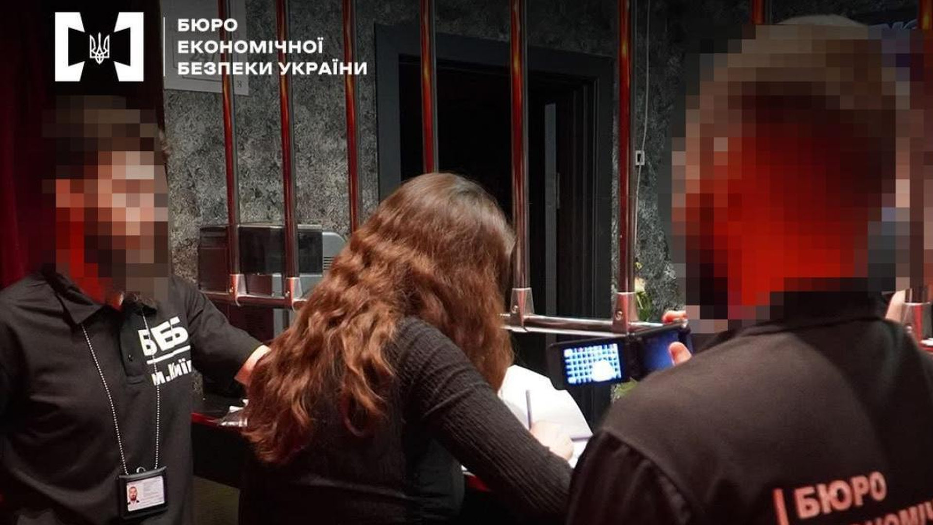 Двоє чоловіків стоять в казино біля жінки, вона стоїть до камери спиною і підписує якісь папери