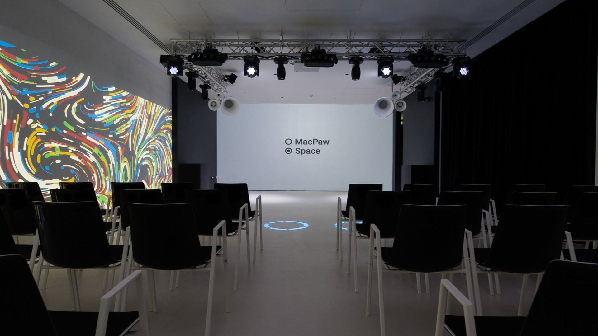 Сучасна конференц-зала з чорними стільцями, проєкційним екраном із написом «MacPaw Space»