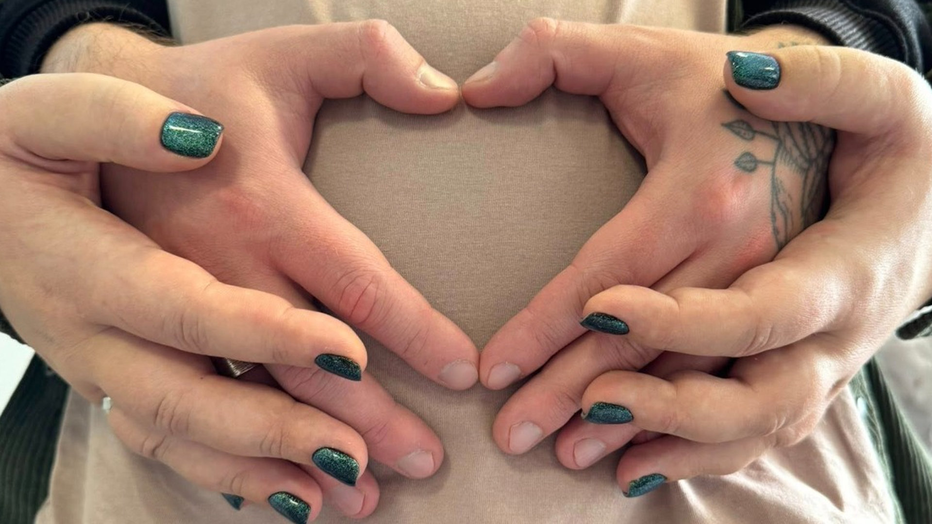 Долоні чоловіка і жінки складені у формі сердечка на вагітному животі жінки