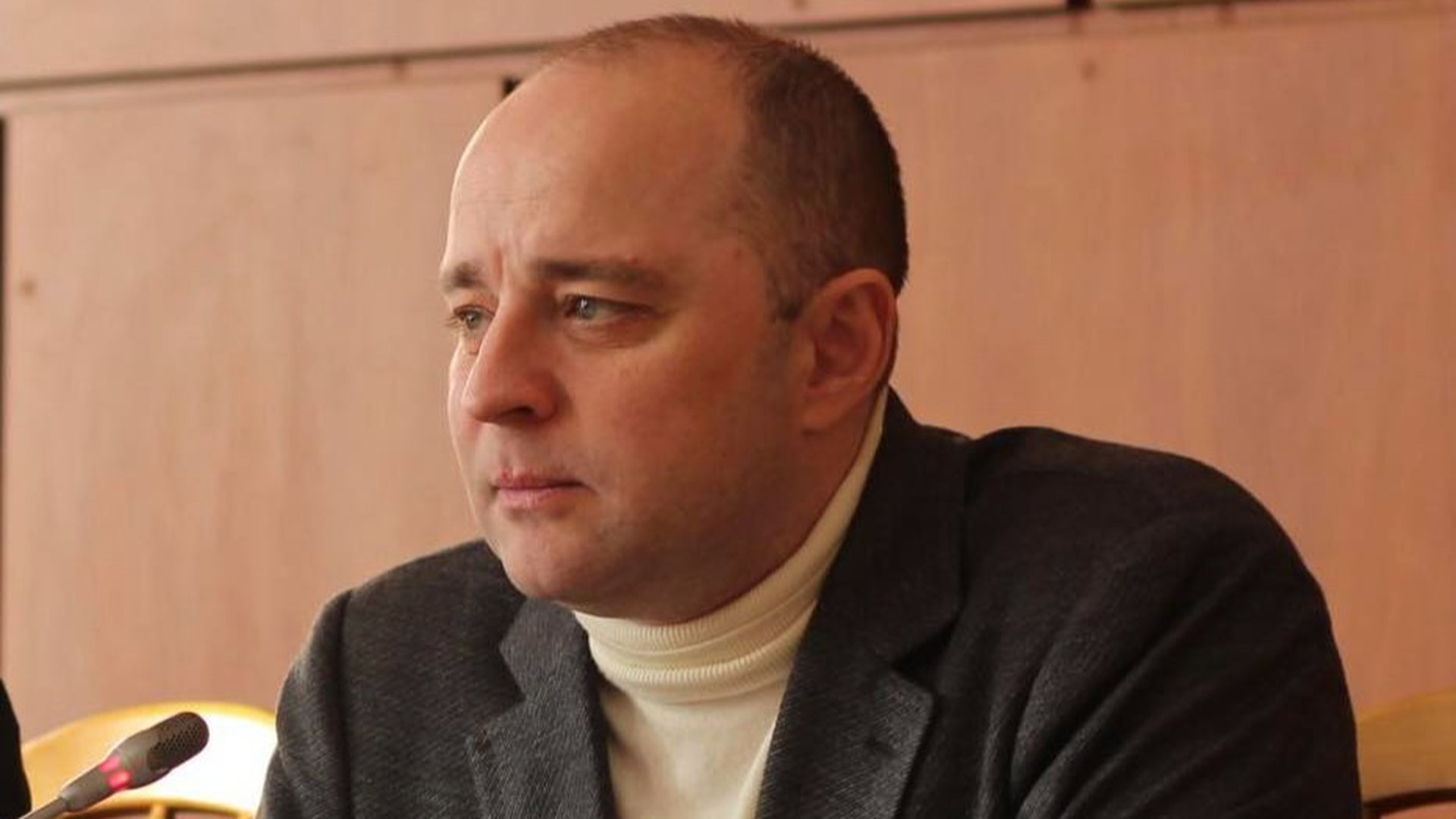 Олексій Момот сидить у залі міськради перед мікрофоном