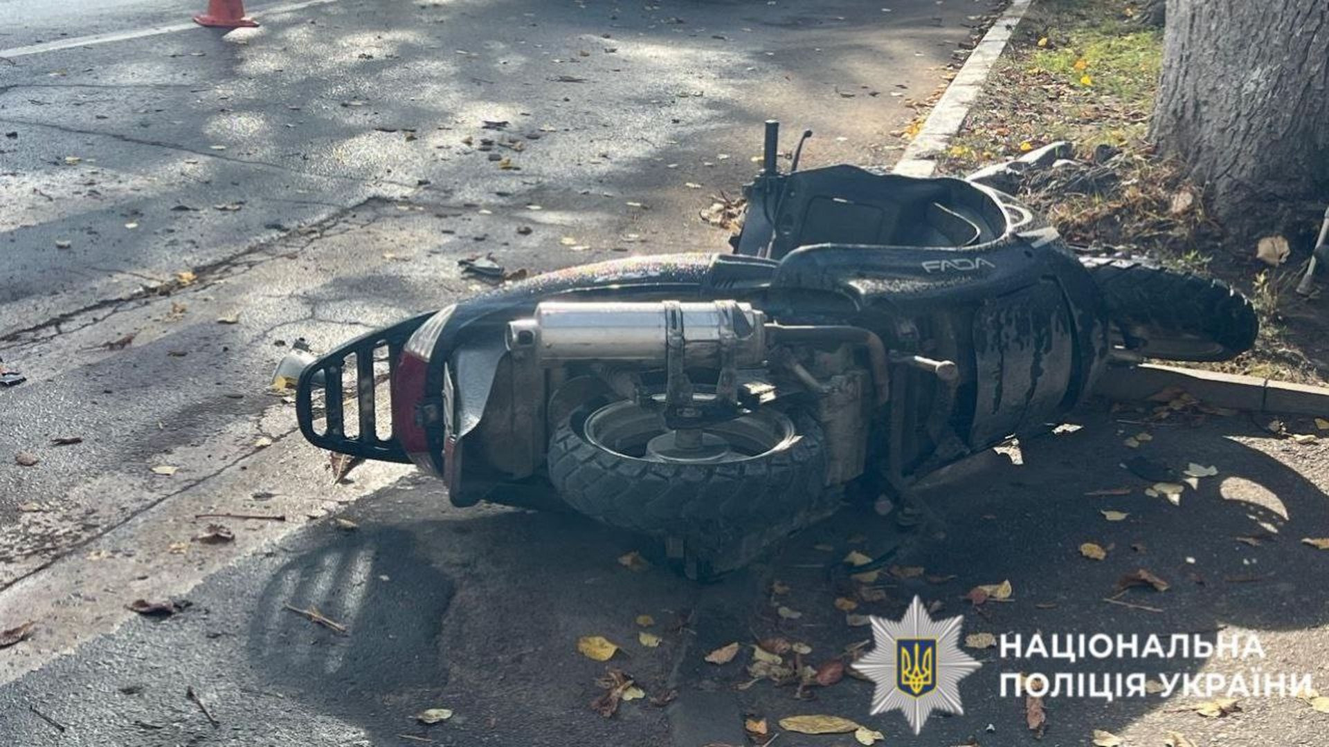 Чорний скутер лежить обабіч дороги, його водійка потрапила в ДТП