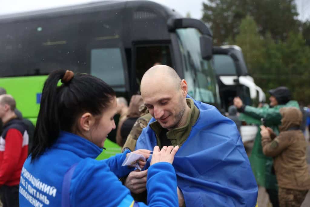 Україна визволила з полону РФ 205 людей: 185 оборонців та 20 цивільних (фото) Українські військовополонених після повернення з російського полону — чоловіки з усмішками, обгорнуті державними прапорами