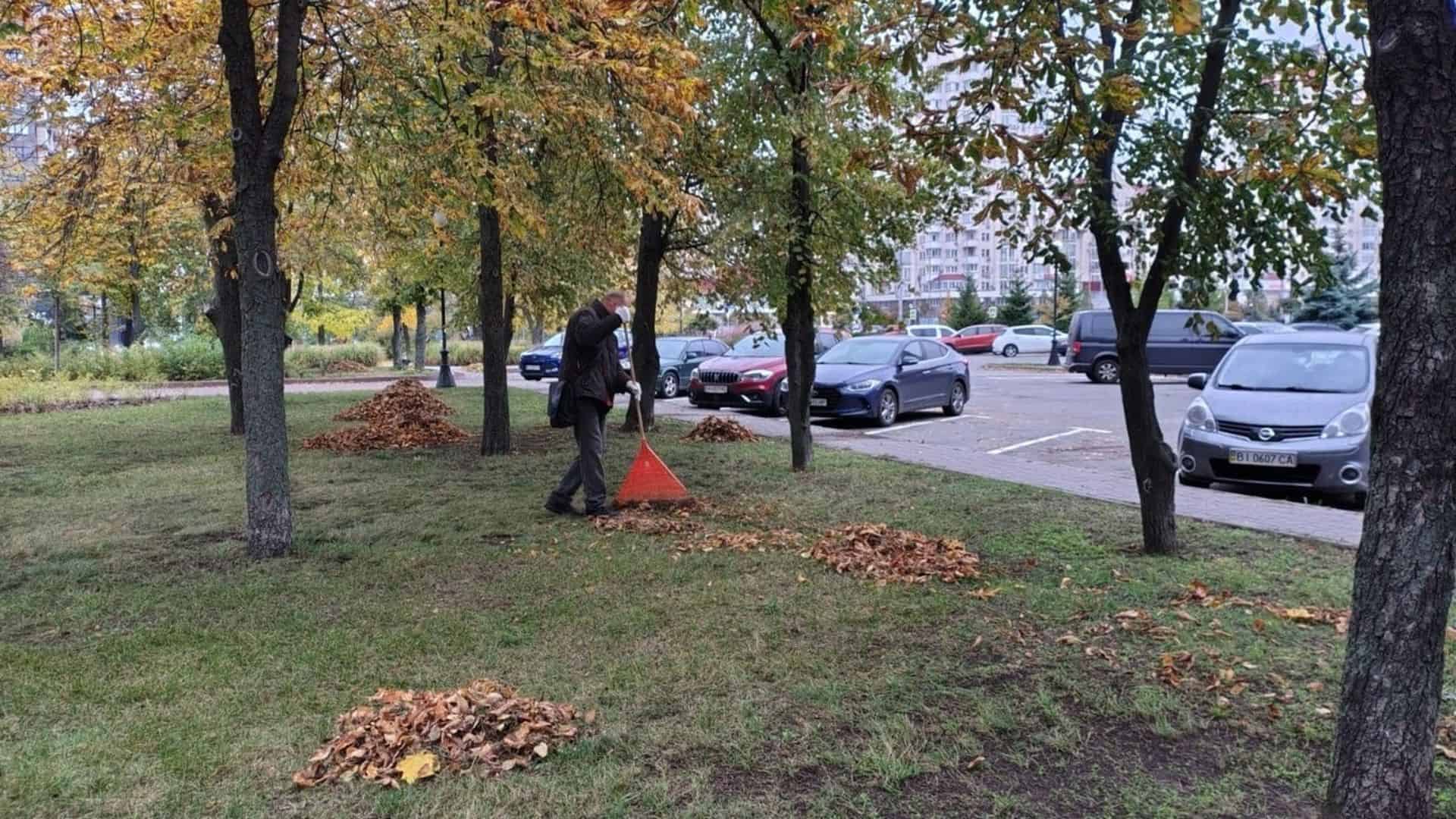 Комунальник збирає осіннє листя червоним совком у міському парку