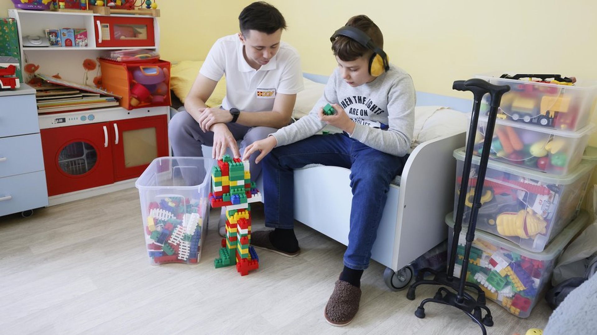 Терапевт працює з дитиною в навушниках, будуючи конструкцію з кольорових блоків у кімнаті