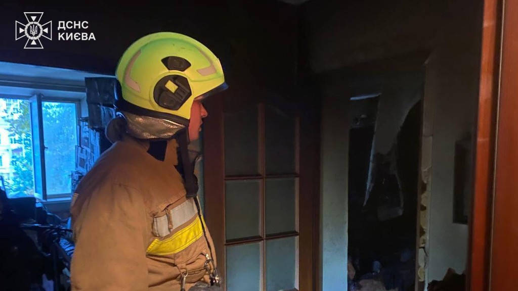 Працівник ДСНС в жовтій касці і захисному костюмі в квартирі де сталася пожежа