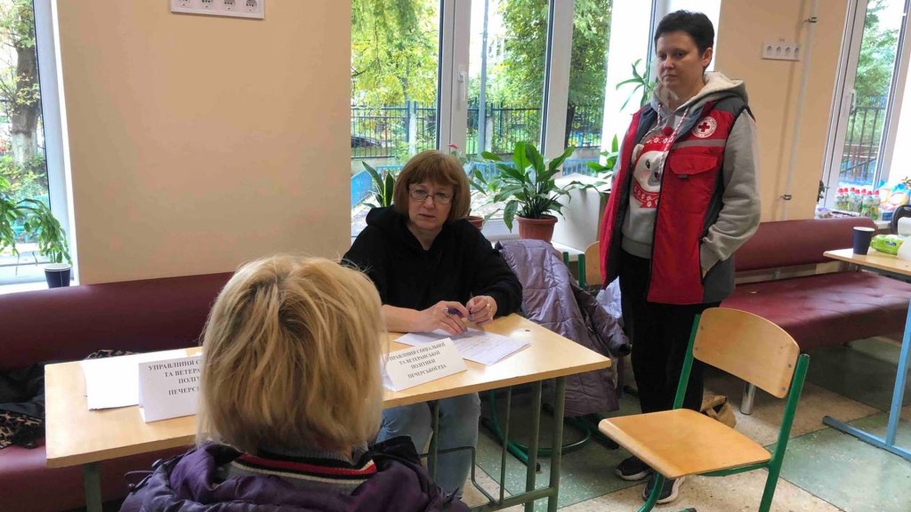 Працівниця управління соцполітики Печерської РДА приймає відвідувачку, чиє житло постраждало внаслідок атаки Росії, поряд стоїть працівниця медичної служби