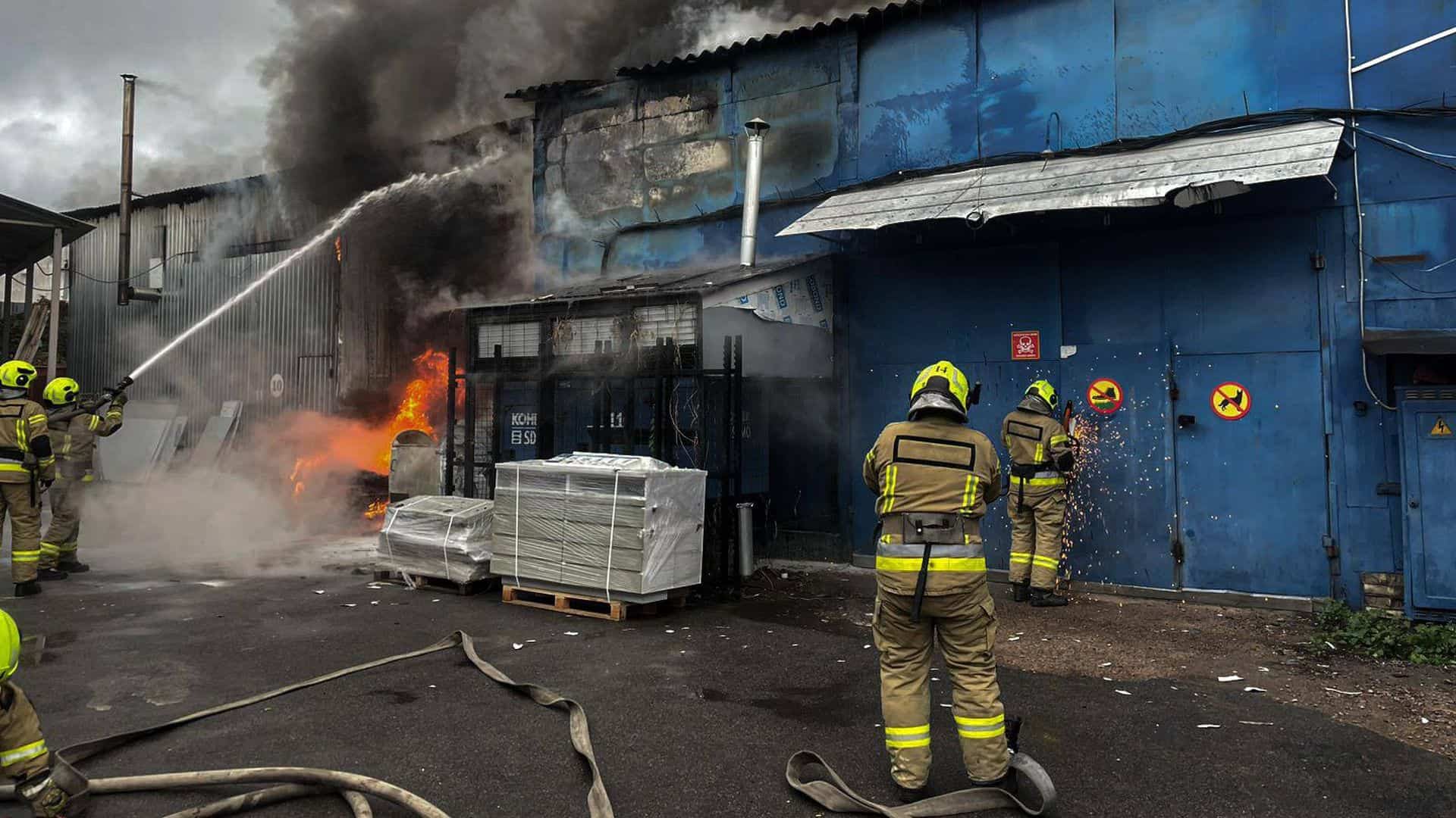 Пожежники гасять полум'я біля синього промислового приміщення з димом