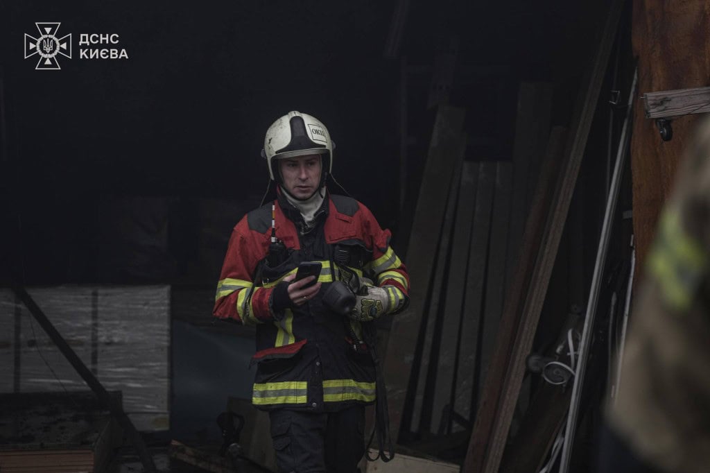 На Подолі загорівся склад на Кирилівській: пожежу загасили (фото) Пожежник у червоно-чорній формі з телефоном біля задимленого приміщення