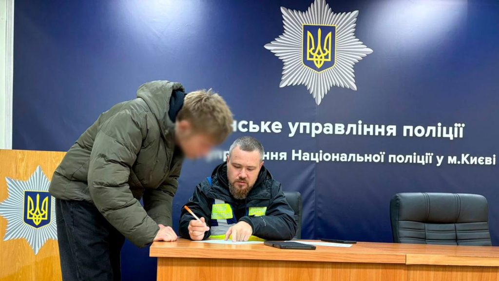 Офіцер поліції сидить за столом, поряд із ним стоїть підліток і ознайомлюється із документом, який йому потрібно підписати 