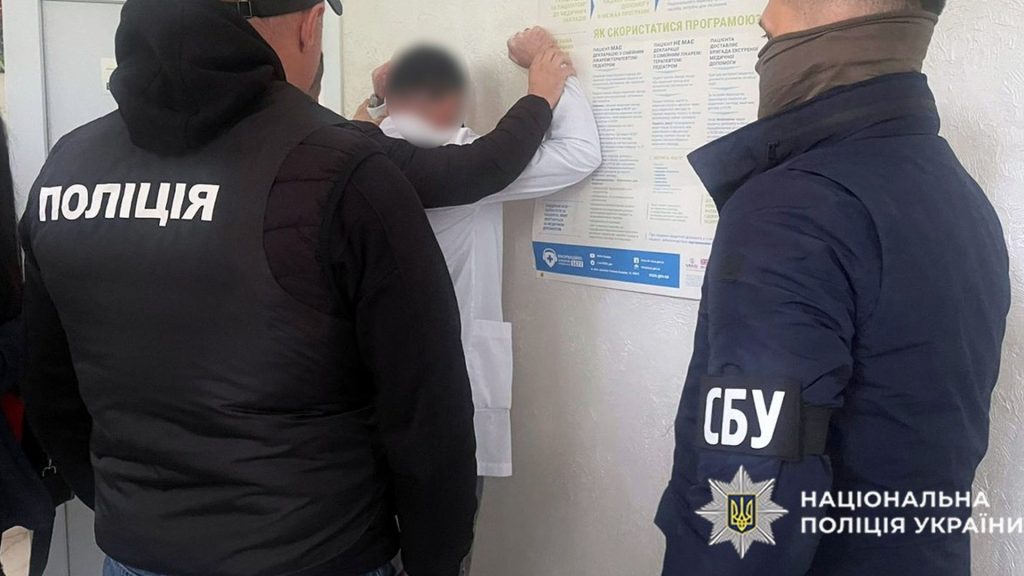 Поліція і СБУ викрили схеми «ухилення»: фіктивні роботи, довідки, виїзд за кордон Працівник поліції і СБУ стоять в приміщенні, біля них ще один чоловік тримає біля стіни чоловіка в білому халаті, ймовірно, підозрюваного