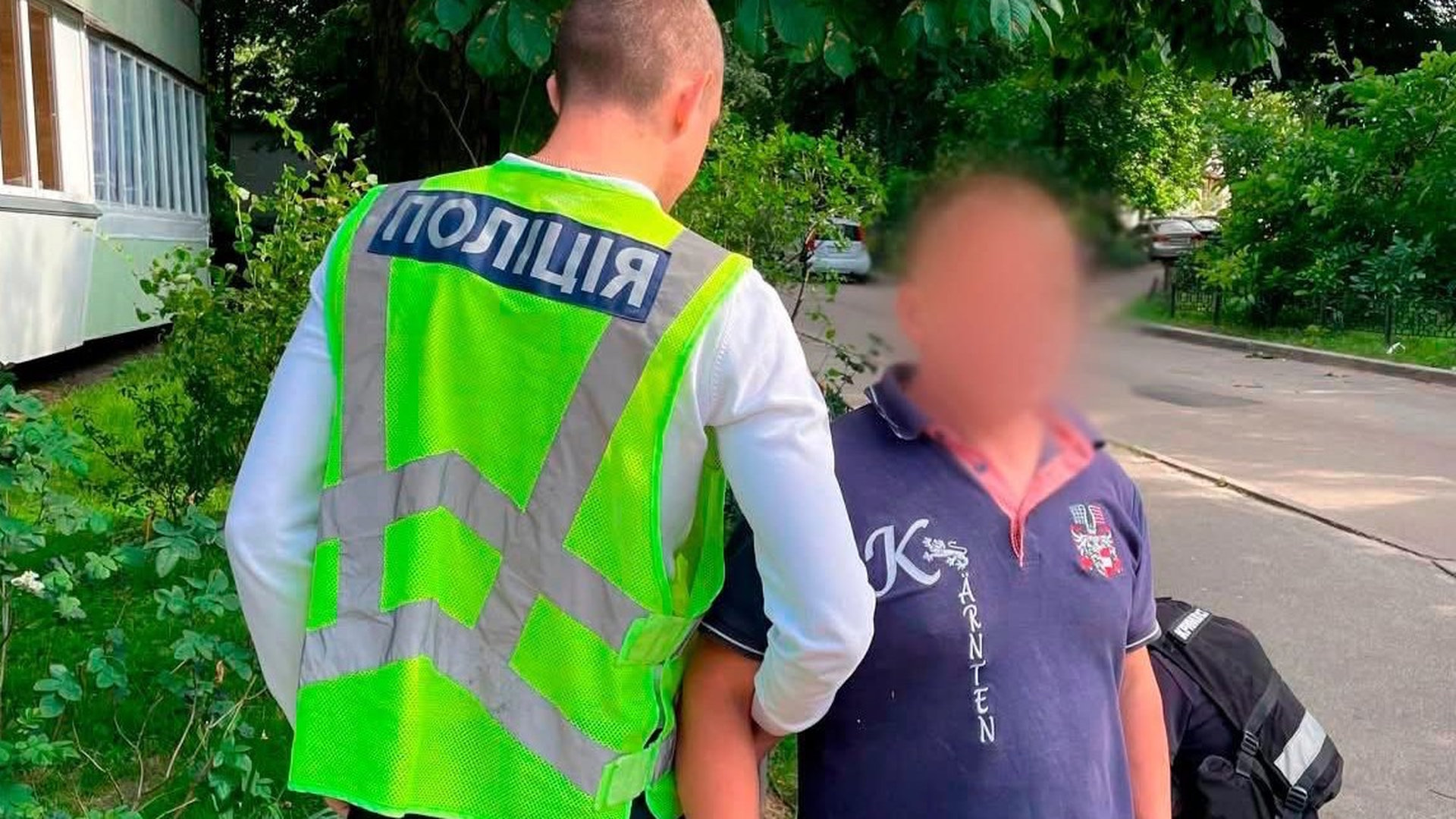 Працівник поліції тримає під руку чоловіка у дворі київської багатоповерхівки, обличчя заблюрене