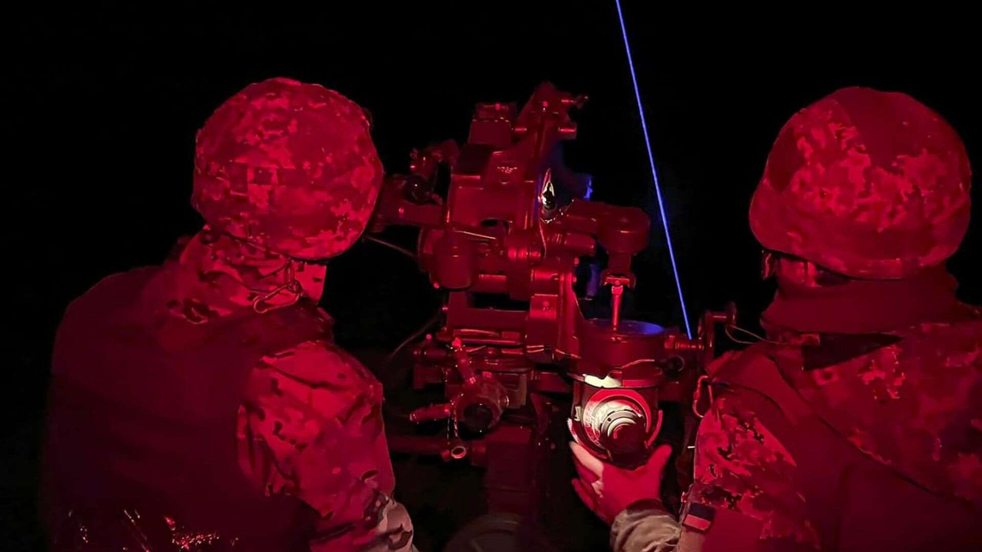 Двоє українських військових у червоному освітленні працюють біля зенітної установки вночі