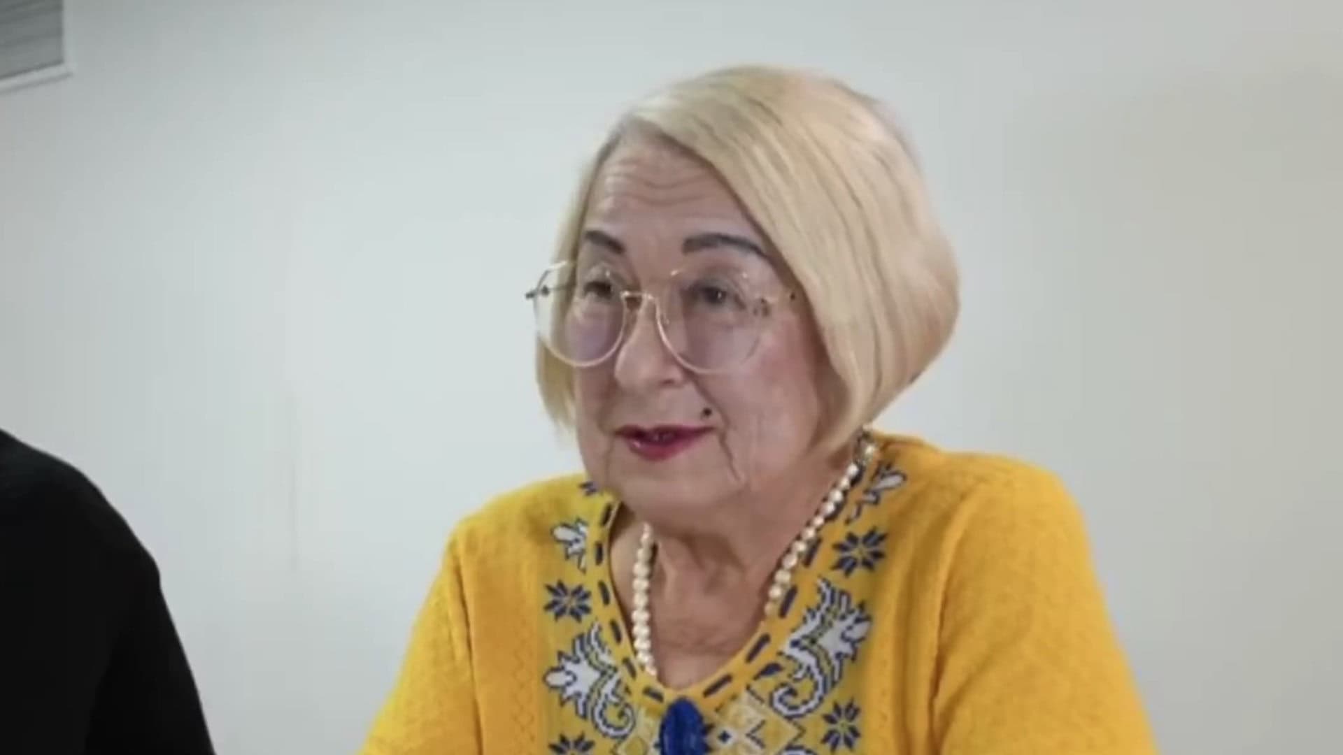 Жінка похилого віку у жовтому светрі з орнаментом дає інтерв'ю