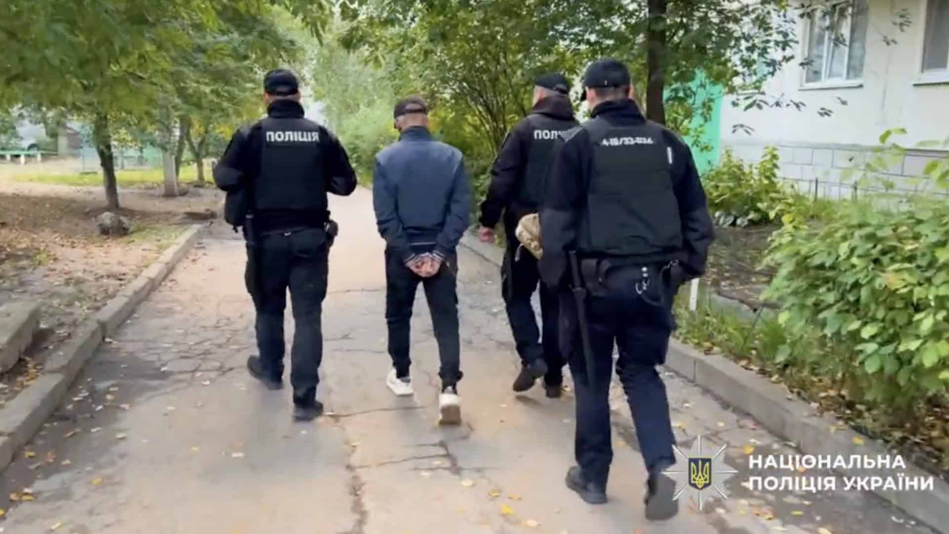 Троє поліцейських супроводжують підозрюваного йдучи вулицею міста