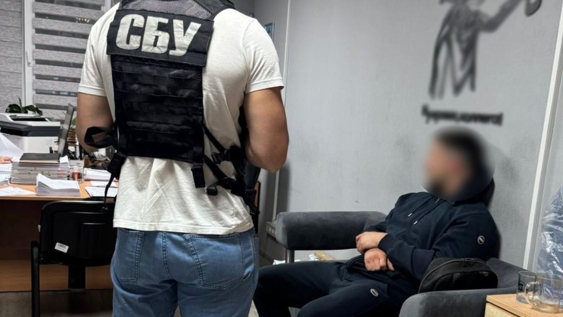 На передньому плані видно працівника у бронежилеті з написом «СБУ», поруч сидить чоловік