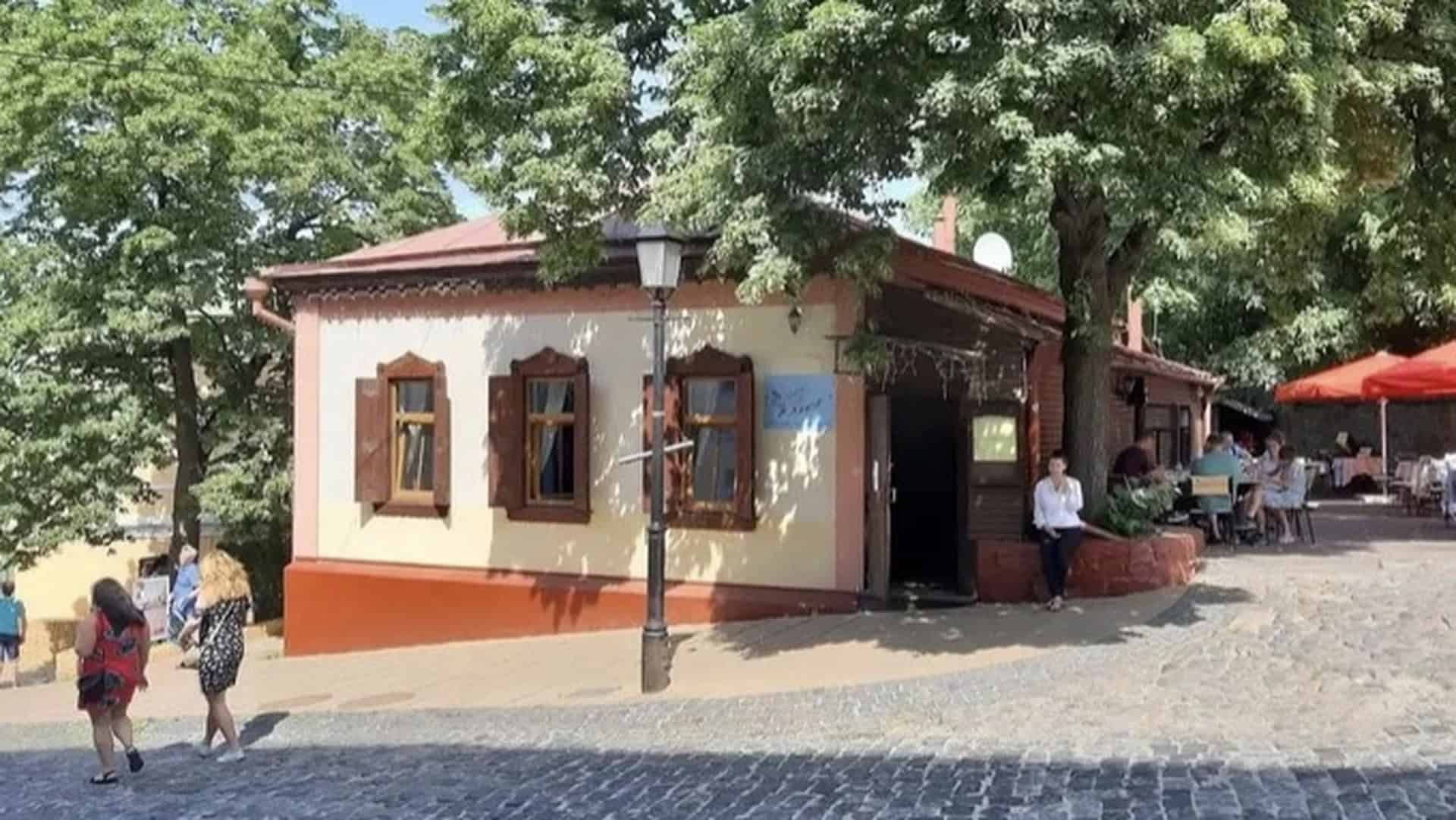 Одноповерхова дерев'яна садиба 1846 року на Андріївському узвозі з коричневими віконницями, бруківкою та зеленими деревами влітку