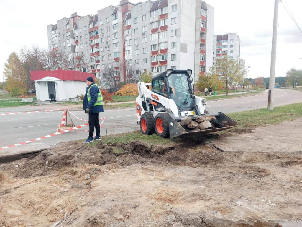 Працівник комунальних служб стоїть біля дороги і будівництва тротуару, там же стоїть невеличкий трактор