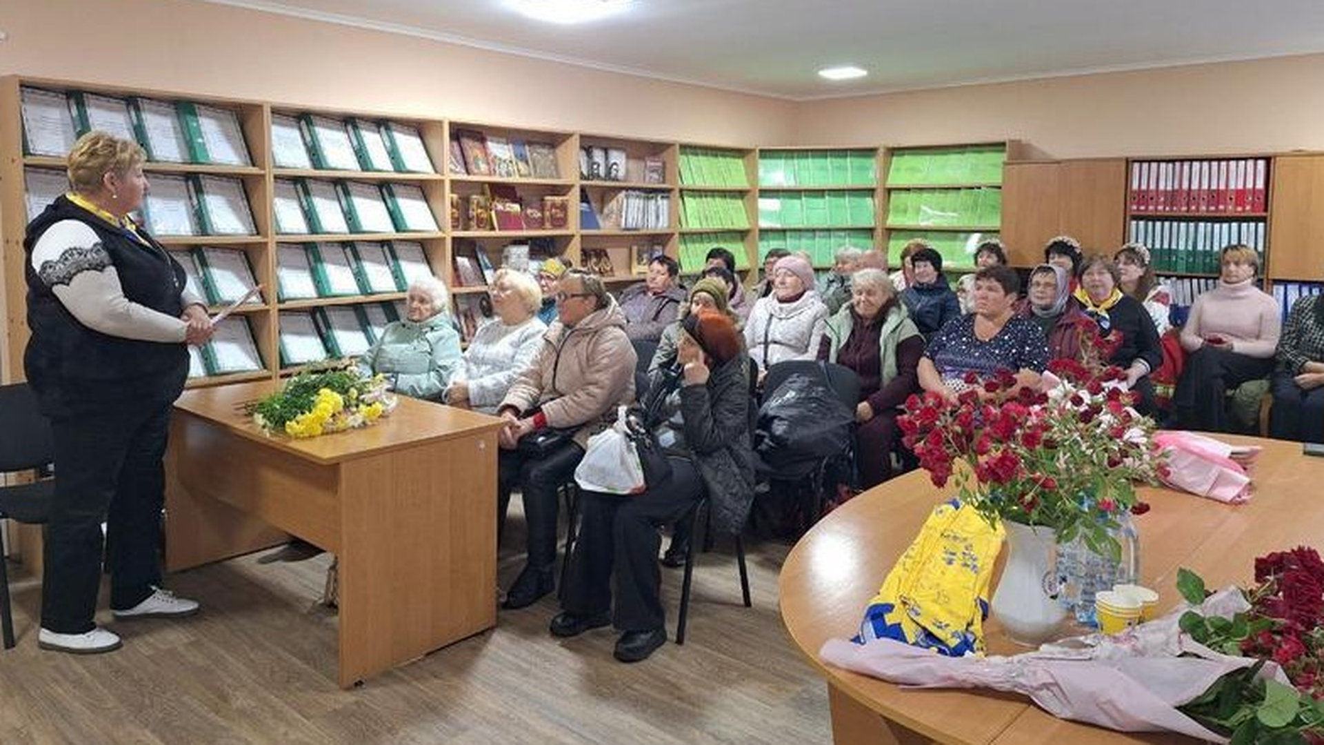 Літні люди сидять за партами в класі, перед ними викладач, вчитель, в класі 15 людей