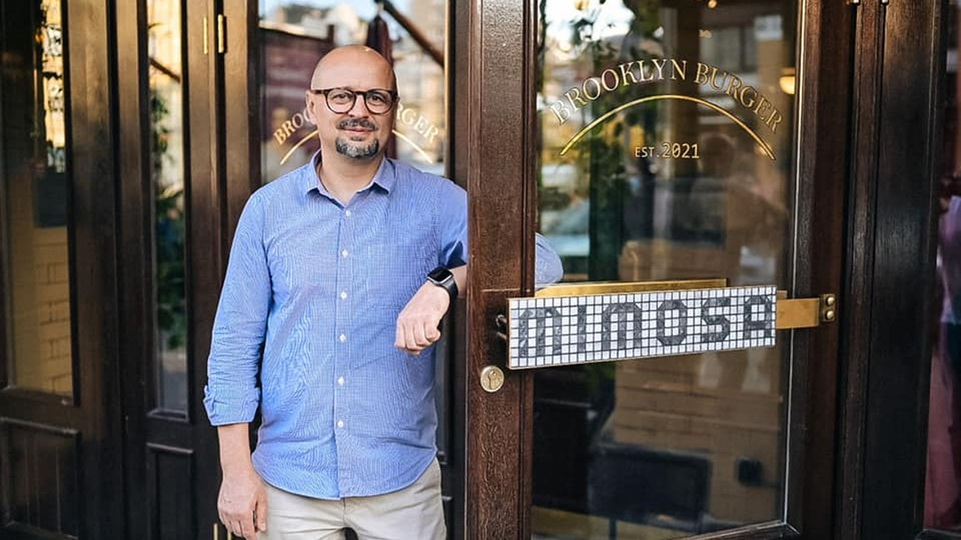 Чоловік у блакитній сорочці та окулярах стоїть біля входу до ресторану