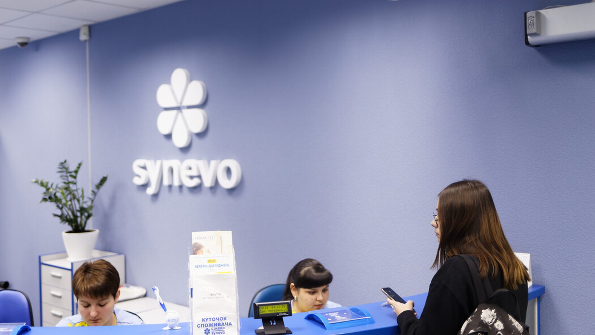 Відділення клініки Synevo з логотипом у вигляді білої квітки на блакитній стіні