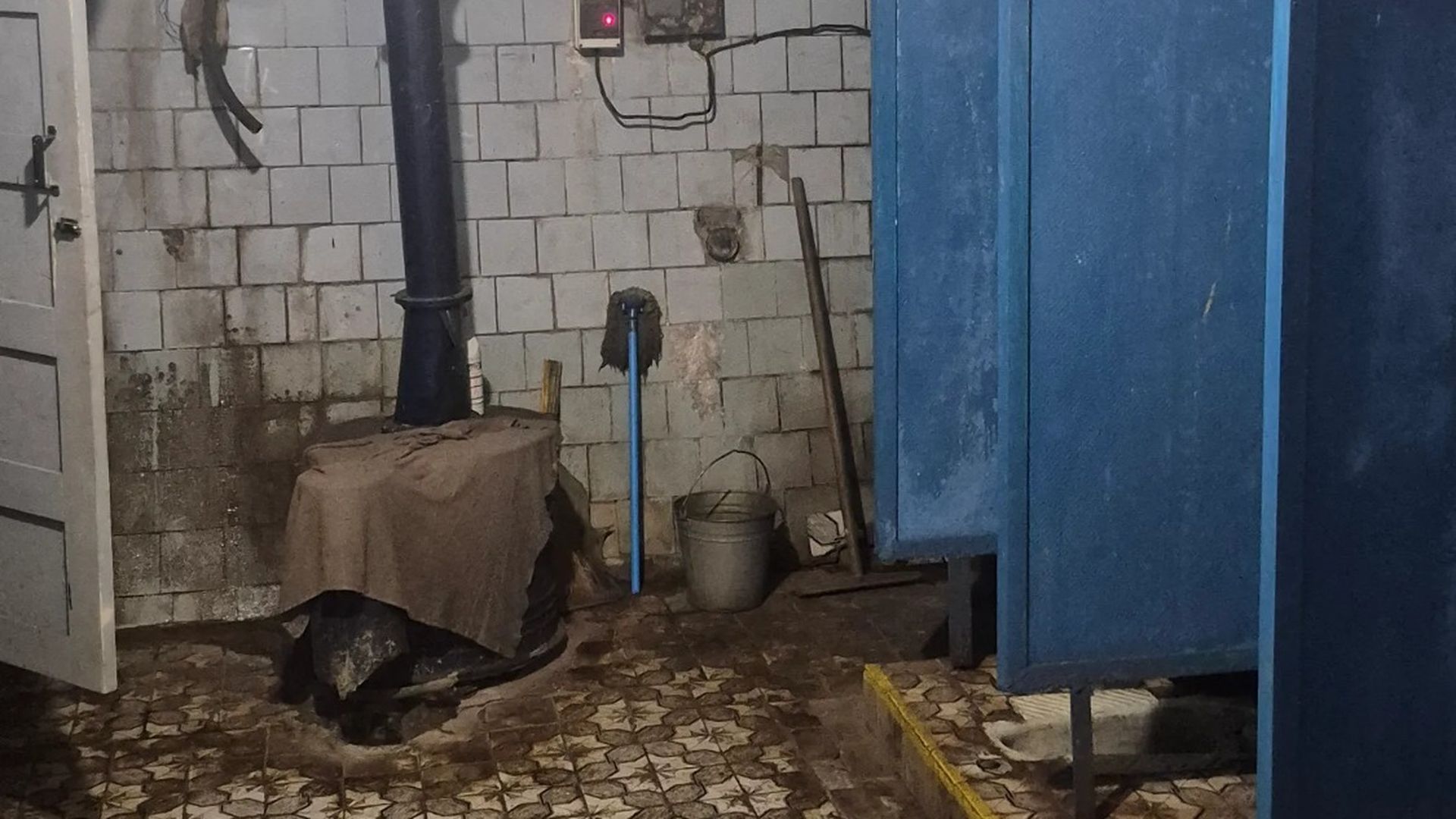 Загальний вигляд санвузла з облупленими стінами, старими кабінками й відром