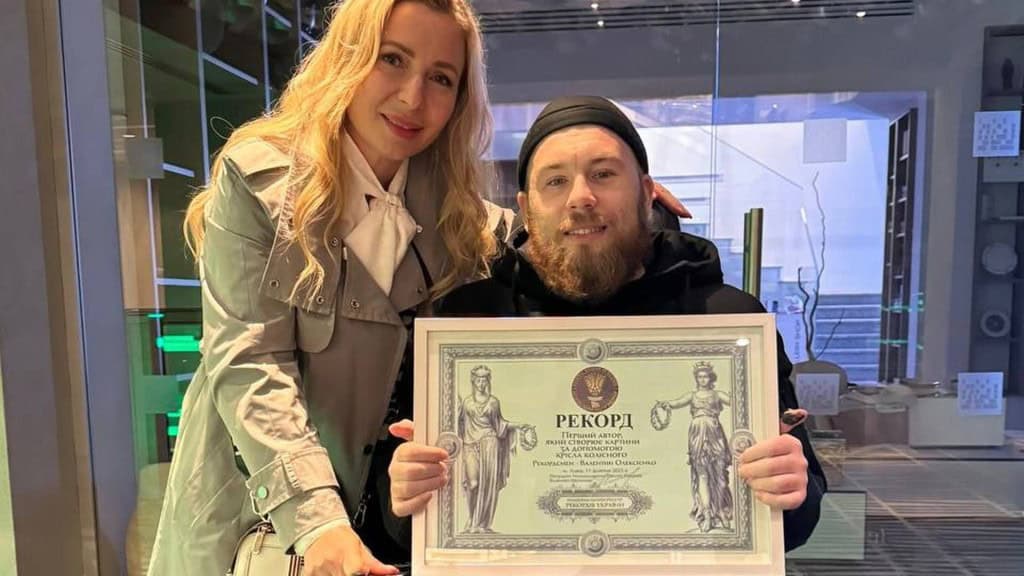 Ветеран малює кріслом колісним і збирає кошти на ЗСУ Ветеран тримає диплом про встановлений рекорд за малювання кріслом колісним, поряд із ним стоїть жінка