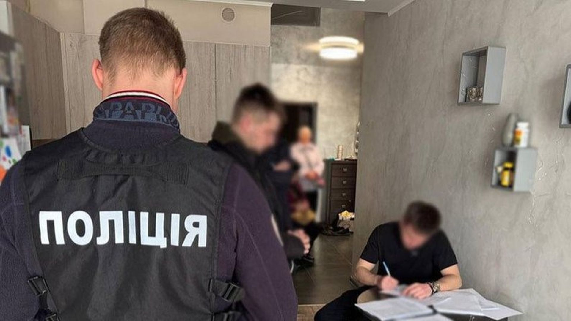 Обшук у квартирі, який проводять поліцейські, один із них у жилеті з написом «Поліція»