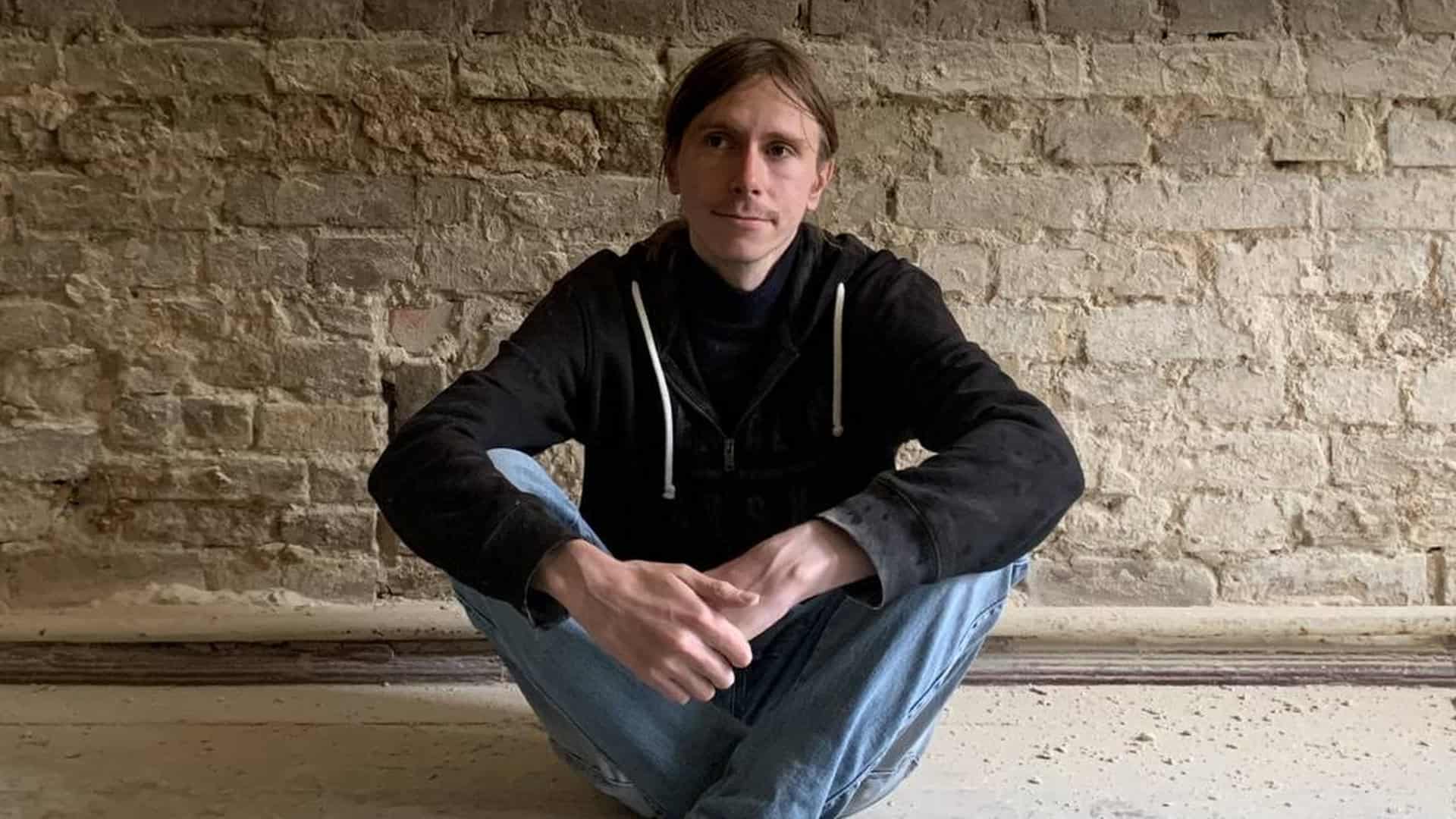 Пам'яткоохоронець Дмитро Перов сидить на підлозі зі схрещеними ногами на тлі старої цегляної стіни