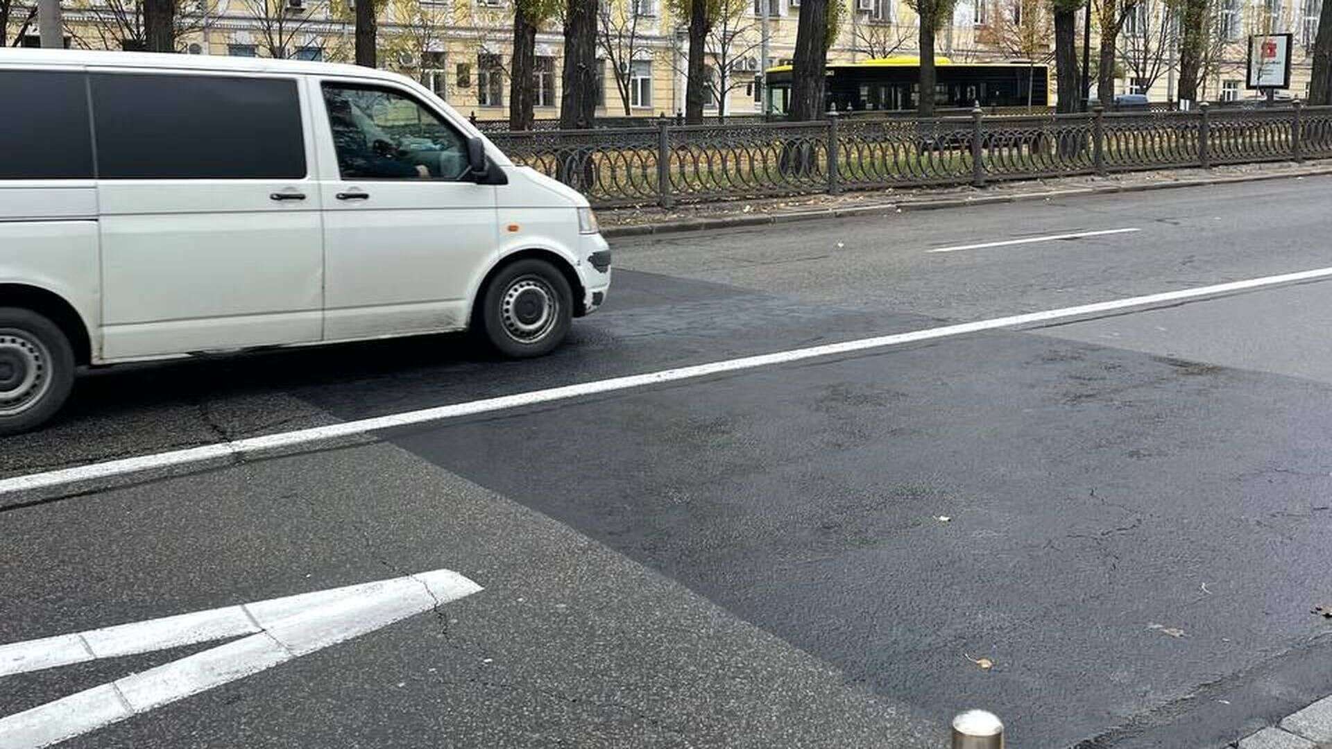 Білий мікроавтобус проїжджає ділянку дороги, де щойно зафарбували дорожню розмітку