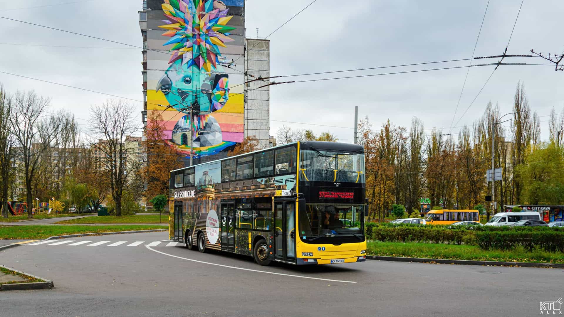 Двоповерховий жовто-чорний автобус проїжджає повз багатоповерхівку з яскравим муралом