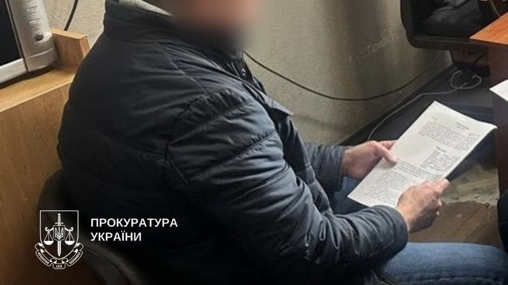 Чоловік в чорній куртці сидить на стільці і тримає папери