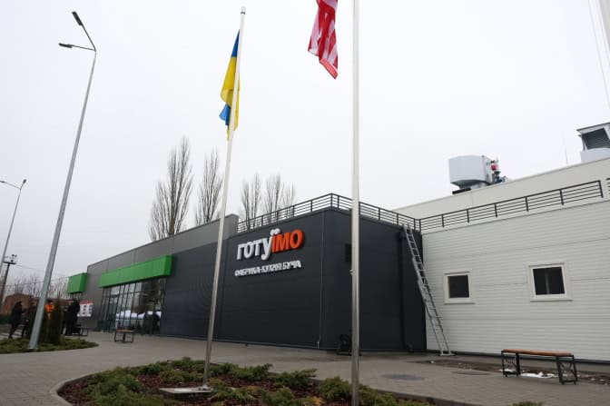 Фасад сучасної будівлі з написом «ГОТУЇМО» та прапорами