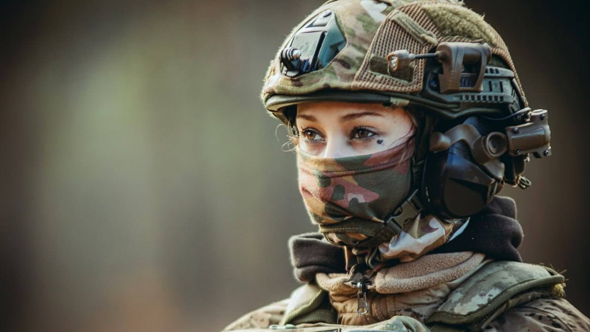 Жінка військова дивиться вдалечінь, її обличчя наполовину закрите балаклавою, вона в касці