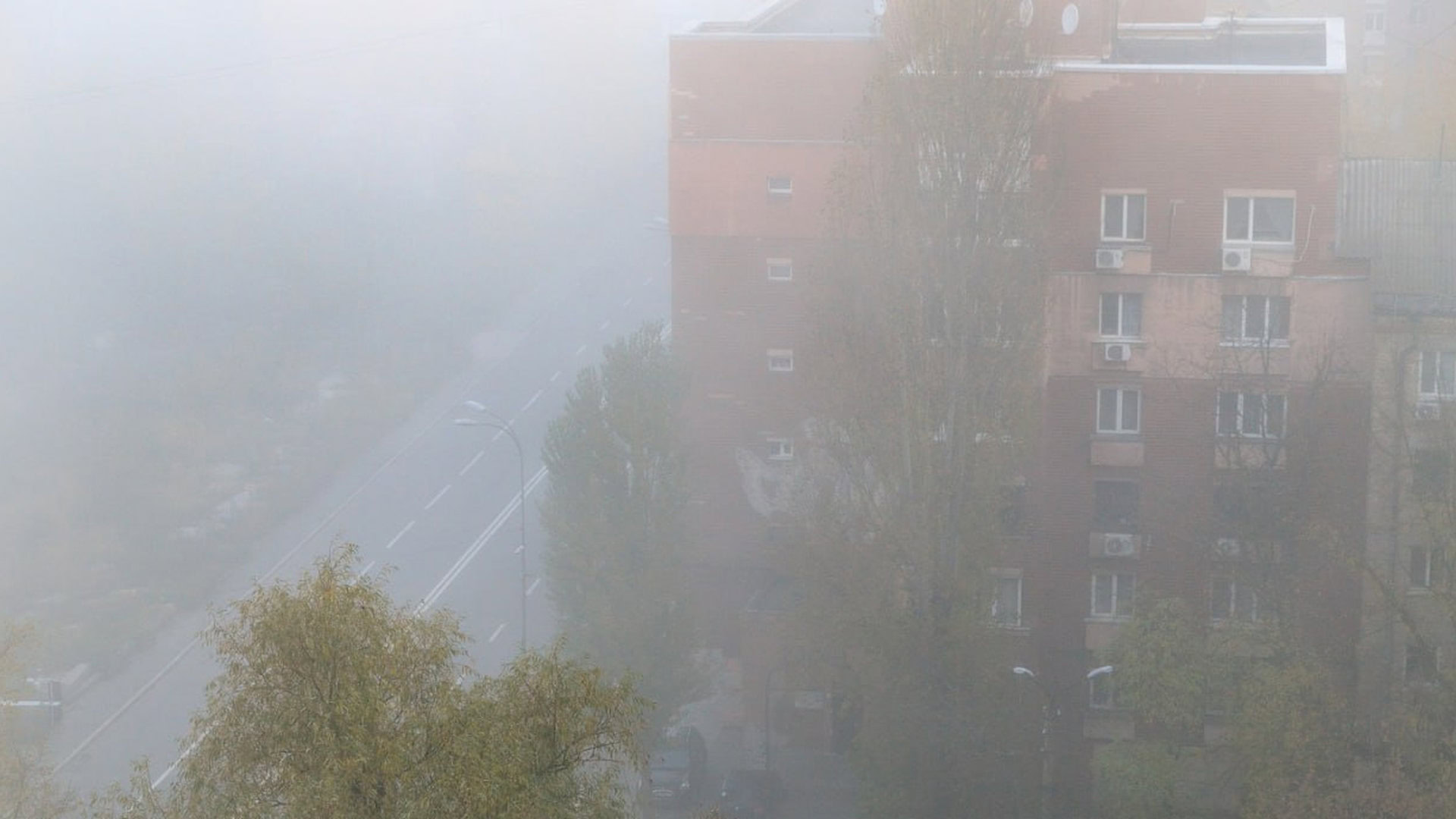 Туман в Києві, в тумані багатоповерхівка і біля неї дорога для автомобілів, яку погано видно через сильний туман