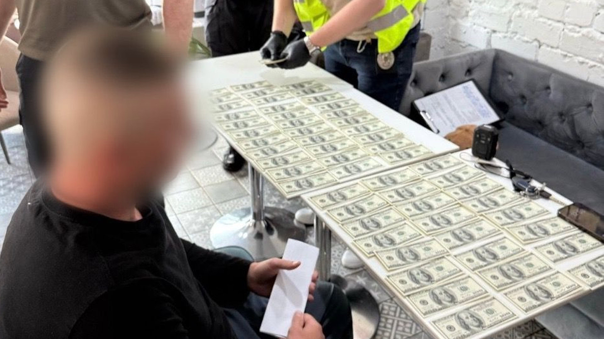 Чоловік із заблюреним обличчям сидить перед столом, на якому розкладені доларові купюри