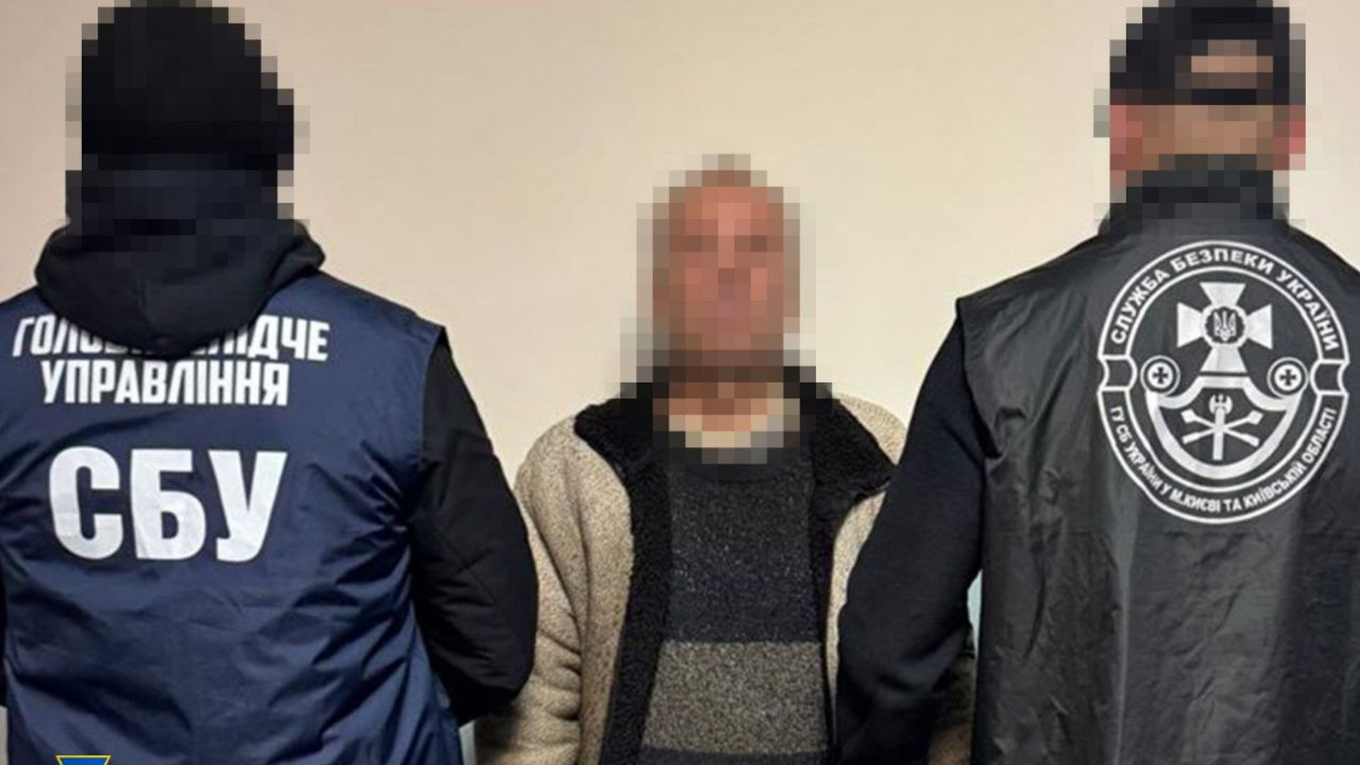 Два працівники СБУ стоять біля затриманого чоловіка, той із заблюреним обличчям