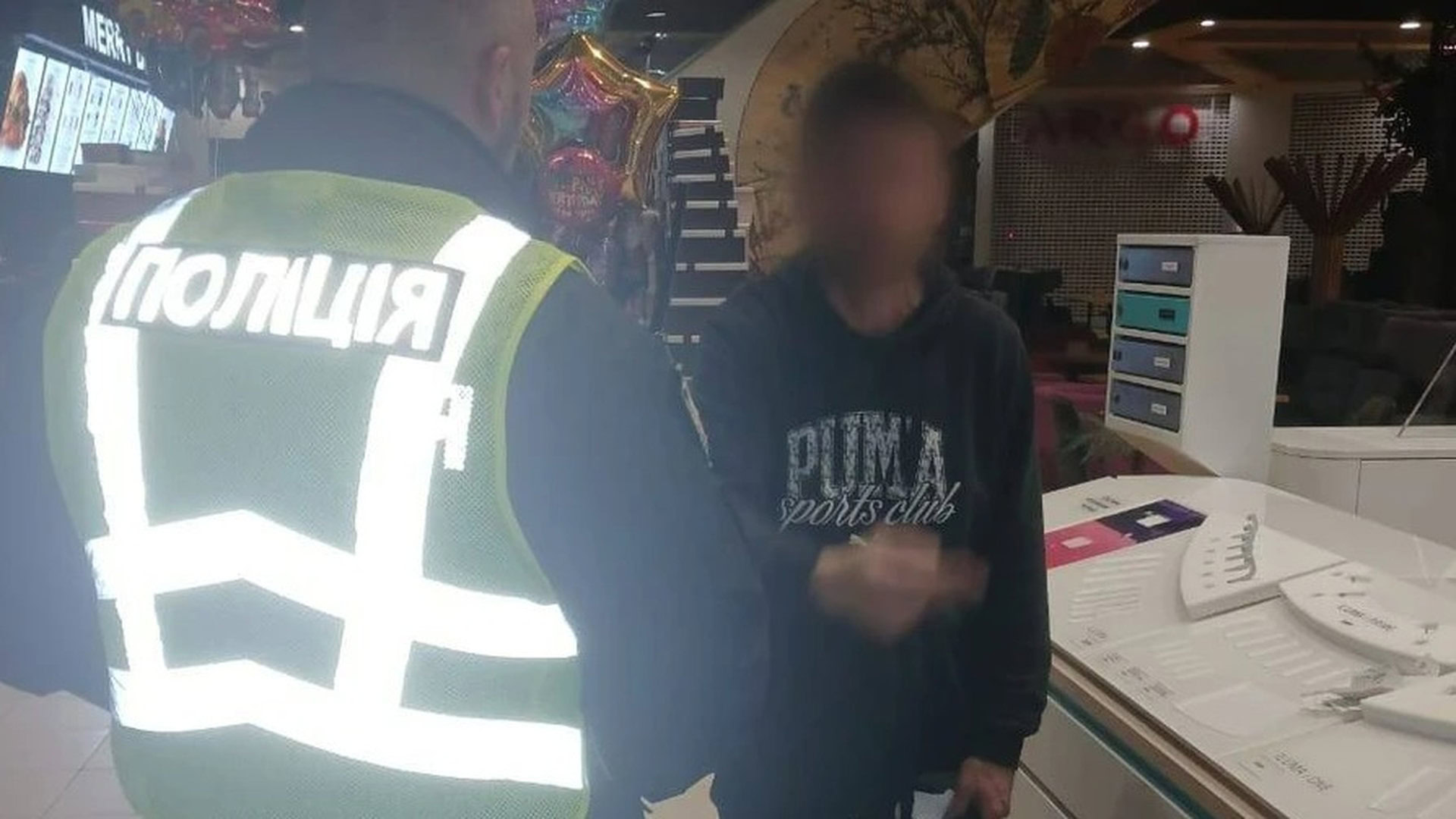 Поліцейський у жилеті спілкується з чоловіком у кофті з розмитим обличчям у ТРЦ