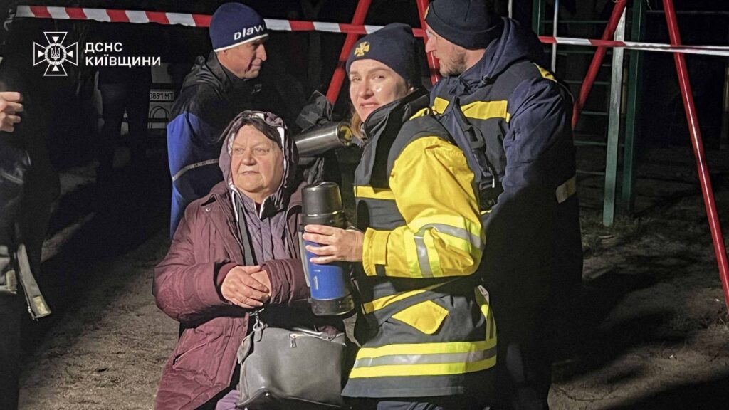 Рятувальники біля жінки, евакуйованої з будинку, пошкодженого російським обстрілом