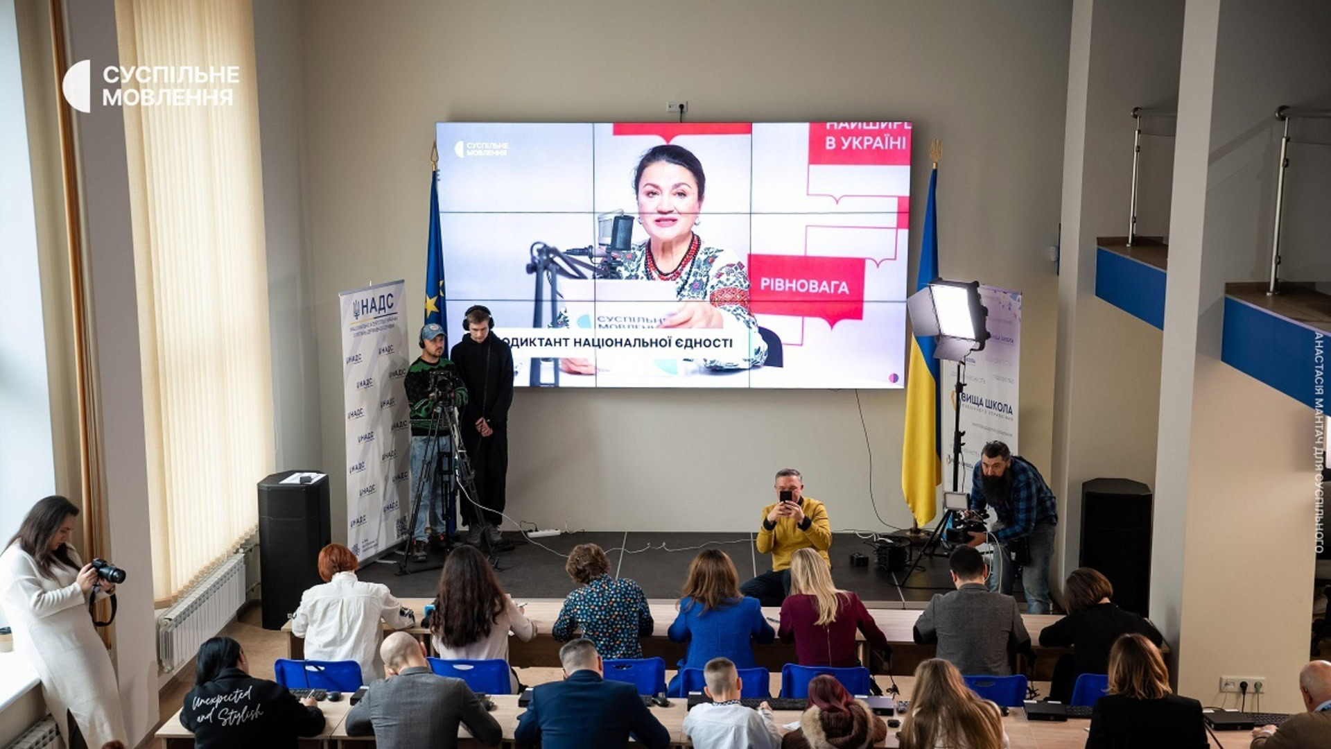 Люди пишуть Радіодиктант національної єдності. На екрані акторка Наталя Сумська читає текст диктанту